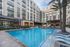 Resort-style pool with palm trees, landscaping, a covered dining/grilling area, a raised fountain, and terraced seating.