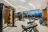 Bank of treadmills, ellipticals, and stair climbers in front of a large window wall with a city skyline view.