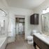 Bright, spacious bathroom with blonde wood cabinets, an attached walk-in closet, a large bathtub, and marble tile on the floors and the bathtub walls