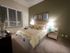 Spacious bedroom with a taupe accent wall, beige carpet, a large window, a king-sized bed, and a dresser.