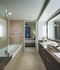 Spacious bathroom with a soaking tub, large dual vanity with a brown quartz countertop, brown cabinetry, and a doorway to a bedroom.