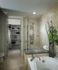 Bathroom with a glass-door walk-in shower, walk-in closet and oval tub with a decorative plant. The marble-style floors and walls are light brown.