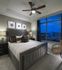 A bedroom with a king-sized bed, ceiling fan, large window, , and white walls with a light grey accent wall. There are three piece of artwork above the bed.