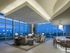Lounge featuring white ceilings, floor-to-ceiling windows, seating area with gray couches and chairs, and a bar area with gray and brown barstools.