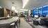 Resident lounge with floor-to-ceiling windows, gray and white seating with a flat-screen TV on the wall, and a bar area featuring gray and brown chairs.