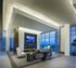 Resident lounge featuring a gray couch and chairs facing a flat-screen TV mounted above an electric fireplace. There are full floor-to-ceiling windows across two walls that showcase a city view.