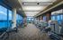 Gym with floor-to-ceiling windows, a TV, a row of stationary bikes, ellipticals, weights, and machines.
