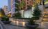 Entrance featuring water wall surrounded by beige stones, trees and plants, and lit up staircase leading to the garden. Apartment homes are featured in the back, and plants line the sidewalk by the street.