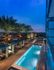 Overhead view of the pool deck from a resident balcony showing a city skyline view, wood floors, palm trees, in-pool lounge chairs, and cabanas