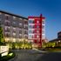 Exterior of the Hanover Alewife apartment building showing the driveway, the red, white and gray facade and trees lining the sidewalk.