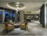 Co-working space with full-width floor-to-ceiling windows, stone floors, desks, tables, and social seating areas with leather armchairs