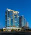 The Hanover BLVD Place high-rise apartment building rising above its neighbors with floor-to-ceiling windows across the width of each floor reflecting the blue dusk sky.