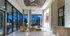 Spacious lobby with a concierge desk, seating area, high ceilings, and a modern chandelier of interlocking rings. There is a view of multiple tall city buildings and trees through the tall full-width windows.