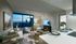 Open-concept living and kitchen space with a couch, two armchairs, a round coffee table with ottomans, a white quartz kitchen peninsula, dark wood-style floors, and a large window.