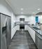 Kitchen with dark wood-style floors, stainless steel appliances, white frameless and handleless cabinets, gray quartz countertops, and an undermount sink with a detachable faucet.