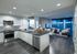 Open-concept kitchen, living, and dining space with dark wood-style floors, white handleless cabinets, stainless appliances, full-width floor-to-ceiling windows, and a gray accent wall.