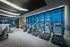 Bank of treadmills, ellipticals, and stair climbers in front of a large window wall with a city skyline view.