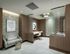 Two desks with rolling leather office chairs are tucked behind textured glass dividers. The room has a loveseat in the foreground, white marble floors, and wood-paneled walls with mosaic insets.
