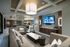 A seating area adjacent to the clubhouse kitchen and dining area with a large wraparound sectional couch in front of an HDTV.