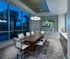 Conference room equipped with an 8-person conference table with rolling white leather chairs, full-width floor-to-ceiling windows, and an HD presentation TV of a mosaic wall.