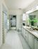 A bright bathroom with a dual vanity, large mirror, white cabinets, a large tub, marble tile on the floor and bathtub walls, and a walk-in closet.