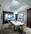 A 8-person conference table with rolling leather chairs in a room with gray and wood-paneled walls, neutral carpeting, abstract art, and an HD presentation TV.
