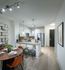 Open-concept kitchen and dining area with white walls, light wood-style floors, a four-person dining table, three barstools at the kitchen peninsula, white cabinets, and stainless steel appliances.