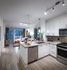 Open-concept kitchen, dining, and living space with white walls, light wood-style floors, white cabinets, stainless steel appliances, and a large window and glass door leading from the living area to the balcony.
