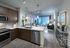 Open-concept kitchen, dining, and living space with ash-gray wood-style floors, dark modern cabinets, stainless steel appliances, white quartz countertops, and a spacious living area with a large window.