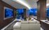 Lounge with dark wood-paneled walls, a large, white leather sectional couch, a flat-screen TV, modern accessories and art, and floor-to-ceiling windows with a city view.