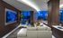 Lounge with dark wood-paneled walls, a large, white leather sectional couch, a flat-screen TV, modern accessories and art, and floor-to-ceiling windows with a city view.