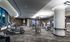 Alternate view of the gym with weight machines, an HDTV mounted on the wall, a full-width mirror wall, carpeted floors, and a bank of treadmills, ellipticals, and stair climbers in front of a large, curved window.