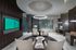 A modern work space with two Mac computers at separate marble desks, a sitting area with 4 chairs in front of an HDTV, and a ring-shaped light fixture mirroring a large circular suspended ceiling detail.