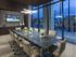 Conference room equipped with 10-person conference table with rolling tan leather chairs, a modern angular light fixture, a full-width floor-to-ceiling window with curtains, and an HD presentation TV.