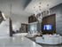 A grand lobby space featuring high ceilings, marble floors and walls, a marble staircase, a modern chandelier of interlocking rings, and a seating area with wood-paneled walls, an HDTV, and two large, white, curved couches.