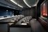 Theater with two rows of large, leather seats and a third row of lecture-hall-style upholstered chairs behind a long desk. There is a projector aiming to a screen in the front, and coffee tables throughout the first two rows.