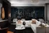 Indoor lounge with a white leather sectional couch, small round coffee tables, and floor-to-ceiling windows overlooking the skyline.