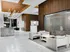 Lobby with four white armchairs next to a glass-walled conference room, marble floors, dark wood-paneled walls, modern silver chandelier, and black marble concierge desk.