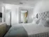 Bedroom with king-sized bed, dresser, walk-in closet, en-suite bathroom, dark wood-style floors, and white walls.