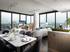 Open-concept living space with dark wood-style floors, 6-seat dining table, and panoramic city view through two full-width floor-to-ceiling windows.