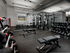 Weight area with dumbbells, barbells, medicine balls, squat rack, power rack, benches, mirror wall, and HDTV.
