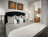 Bedroom with a king-sized bed, a modern standing lamp, side table with a small lamp, modern artwork on the wall, and an entrance to the bathroom.
