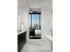 Bathroom with white marble walls, a soaking tub, dark wood cabinetry and white quartz countertops. There is an entrance to a bedroom with windows overlooking the city.