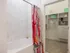 Bathroom with an oval soaking tub, floral shower curtain, and marble tiling to the ceiling. A door leads into a large walk-in closet with beige carpet.