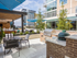 An outdoor grilling and dining area with a four-seat patio table, traditional stainless steel grill, and a Big Green Egg charcoal and ceramic grill. The prep spaces have granite countertops.