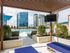 A wooden cabana space with two upholstered lounge chairs overlooking the pool and city skyline, enclosed by a raised landscaping bed with bushes.