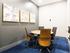 A private meeting area with four rolling chairs around a table, bright blue carpeting, and abstract art on the walls.