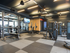 A gym with large windows, bench and squat racks, machines, and a wall of mirrors.