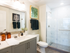 Bathroom with a glass-walled walk-in shower with floor-to-ceiling marble tile, a white quartz countertop with gray cabinets, and a large framed mirror.