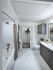 Bathroom with a large tub, dark wood cabinets, an attached walk-in closet, and marble tile on the floor and bathtub walls
